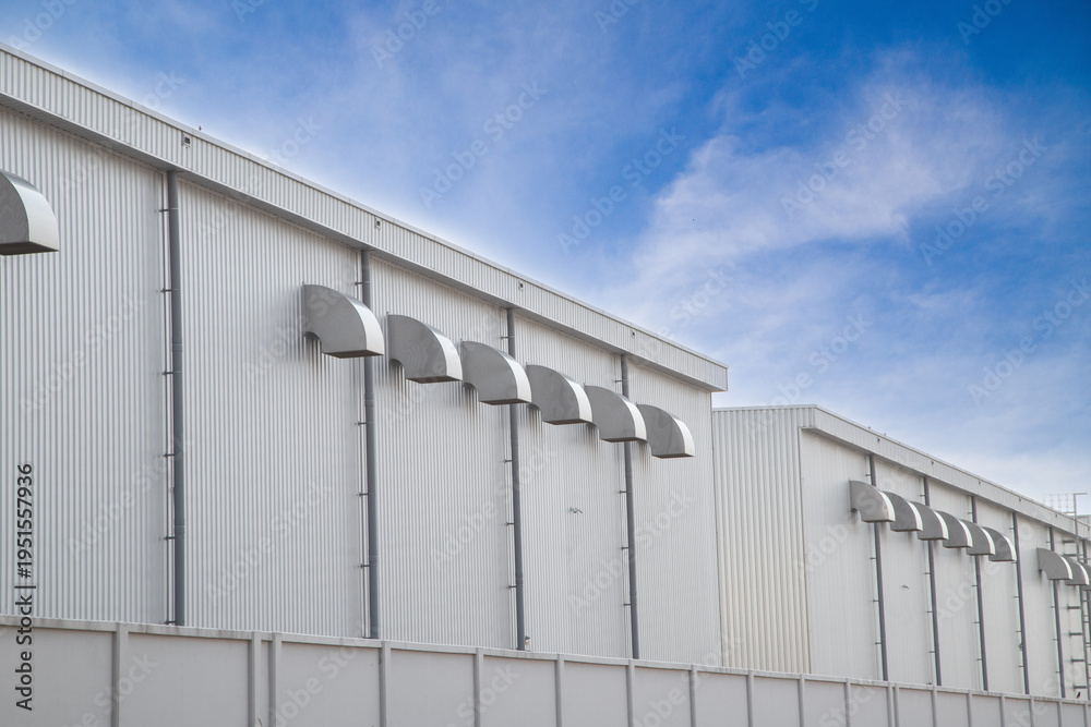 Obraz premium Rows of industrial ventilation ducts on a modern metal warehouse wall under blue sky.ndustrial air conditioning and ventilation system for energy-efficient factory building.
