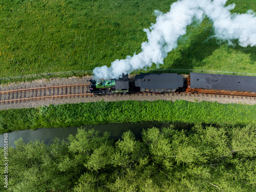 Aerial view of a vintage steam train chugging along the tracks, plumes of white smoke billowing against the lush green fields, Benningbroek, Noord-Holland, Netherlands.