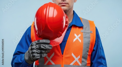 Man in orange safety vest holding red hard hat on blue background
