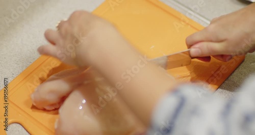 A woman with jewelry cuts a chicken carcass on an orange chopping board