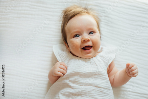 Smiling cute infant baby lying on a white textured blanket 