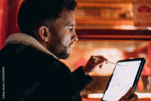 Foto Close up of man drawing on tablet with stylus at night, male designer focused on digital artwork, 5G wireless internet technology, remote work, digital nomad life, authentic representation, profile