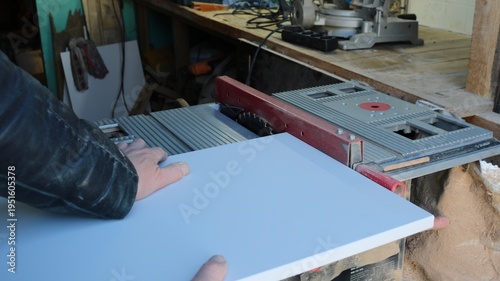 In a woodworking shop, a carpenter clamps a board to the tabletop of a running circular saw to cut a piece, a technique used to cut building materials on a miter saw, cutting material on a power saw