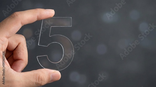 A hand gently holds a pristine, clear number five against a dark, bokeh-filled background, symbolizing a key milestone, ranking, or an important count