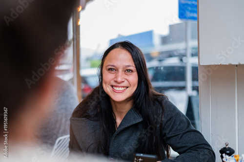 Woman sitting in a cafe table smiling towards the person in front of her