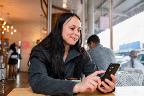 Woman sitting in a cafe table with a cup of coffee engaged on her phone