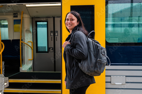 Woman waits at the train door in Wellington, New Zealand, carrying a backpack and smiling