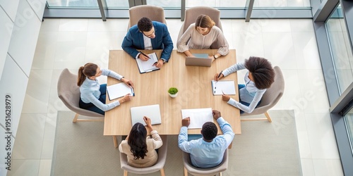 Negotiation Five diverse professionals collaborating around a table in a modern office setting with laptops and documents.