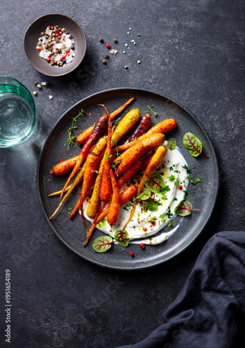 Roasted carrots salad with yogurt. Dark grey background. Top view.