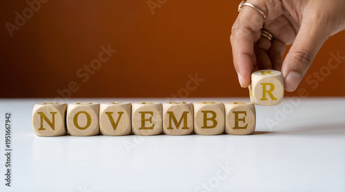 A hand carefully places the final wooden letter 'R' to complete the word 'NOVEMBER', symbolizing the arrival or planning of the eleventh month and upcoming seasonal activities