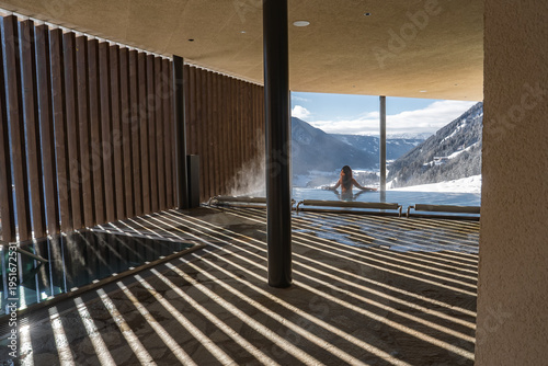 Принти на полотні A person relaxes in a steaming infinity pool as low winter sun casts striped shadows on a modern spa terrace in the Dolomites, northern Italy, with jagged peaks and snow