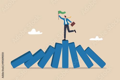 A business leader stands triumphantly atop a row of falling dominoes holding a small green flag