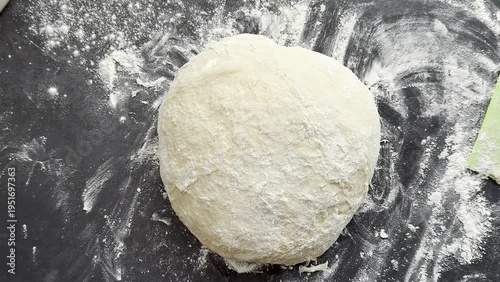 Dough ball covered in flour placed on a dark countertop with scattered flour, showing the preparation stage for baking bread in a kitchen setting