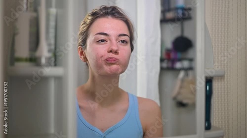 A woman rinses her mouth while looking in the mirror