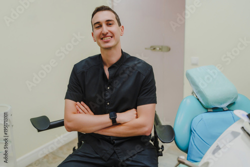 The smiling doctor in the dentist's office. Specialist in oral cavity treatment. A doctor in a black uniform. A doctor with a watch on his right hand.