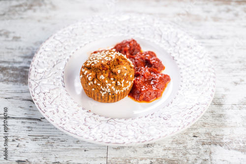 Proja sprinkled with sesame, served on a decorative white plate with a side of ajvar.