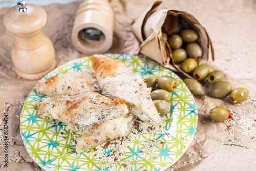 Roasted pieces of chicken served on a colorful plate, with the addition of olives and spice grinders in the background.