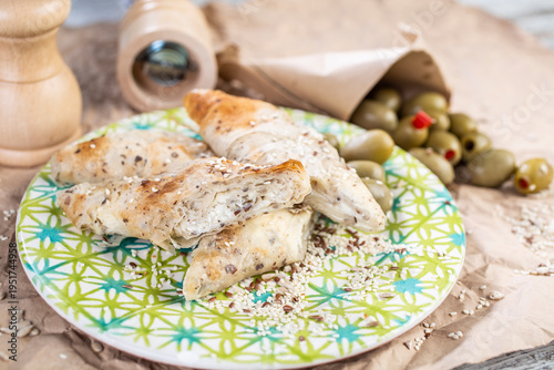 Roasted pieces of chicken served on a colorful plate, with the addition of olives and spice grinders in the background.
