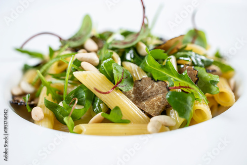 A portion of penne pasta served with black truffle leaves and fresh rocket on a white plate.