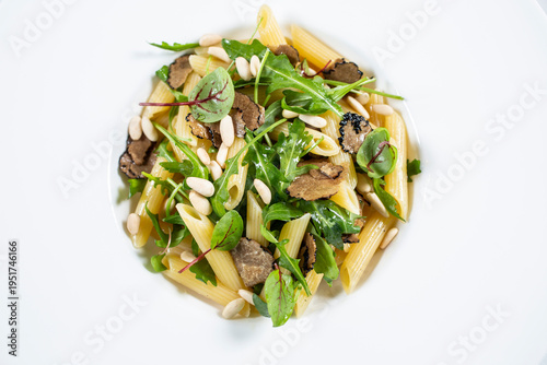 A portion of penne pasta served with black truffle leaves and fresh rocket on a white plate.