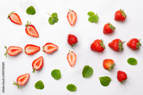 Strawberries, halved strawberries, and leaves on a white background.