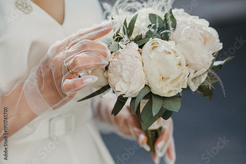 The bride holds a bouquet in her hands. The bride's hands are in gloves.