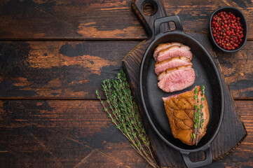 Seared duck breast sliced and served in cast-iron skillet with thyme on rustic wooden background ideal for gourmet food photography.