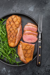 Gourmet grilled duck fillet with crispy skin and tender slices served on black plate over textured dark surface ideal for food photography.