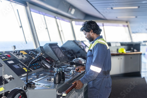 Deck officer standing at the navigation console supervising vessel operations at sea.	