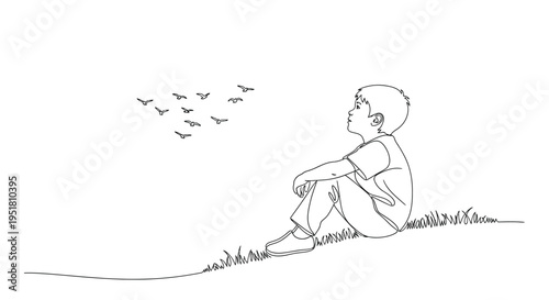 A young boy sits in grass gazing upwards at a flock of flying birds