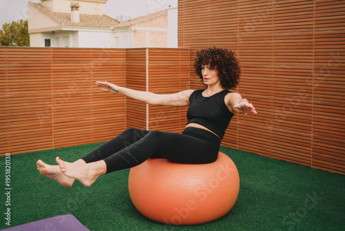 Woman practicing on rooftop. Female performing balance exercise on rooftop turf in sunlight