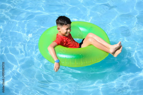 Happy young boy floating with a green inflatable ring in a swimming pool