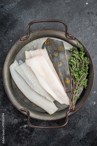 Photos Raw flounder flatfish fillets with skin and thyme on metal tray on dark backgrou