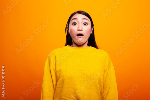 Fotografi Young woman in a yellow sweater shows a surprised and fearful expression, with wide eyes, staring in awe