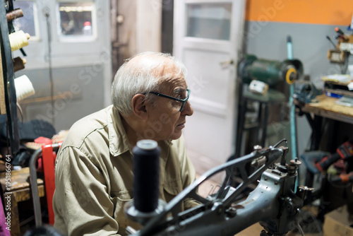 Принти на полотні Elderly Latino upholsterer focused on repairing a backpack with a sewing machine