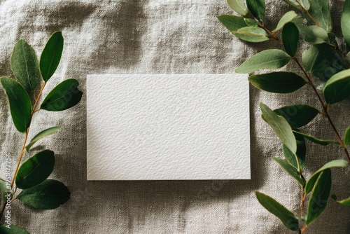 Card rests atop textured cloth, flanked by verdant eucalyptus branches, soft light