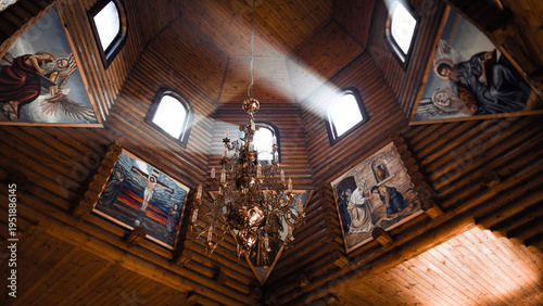 Atmospheric interior of a wooden Orthodox church with sunbeams through windows and chandelier.