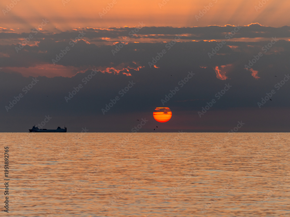 Naklejka premium Merchant ship during sunrise over the Mediterranean Sea seen from the beach in Torremolinos. Costa del Sol, Spain