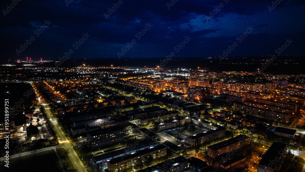 Naklejka premium Aerial drone footage of a small provincial town in Poland at night, glowing street lights, quiet urban landscape, peaceful atmosphere, and illuminated roads under dark sky.