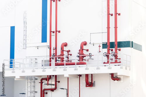 Red pipes and valves delivering essential services on the white exterior of an industrial building with architectural details