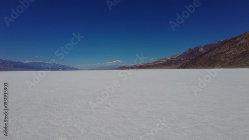 A steady panoramic sweep across the expansive white salt flats of Badwater Basin. Scenic desert landscape featuring the contrast between the white valley floor and the towering brown mountains.