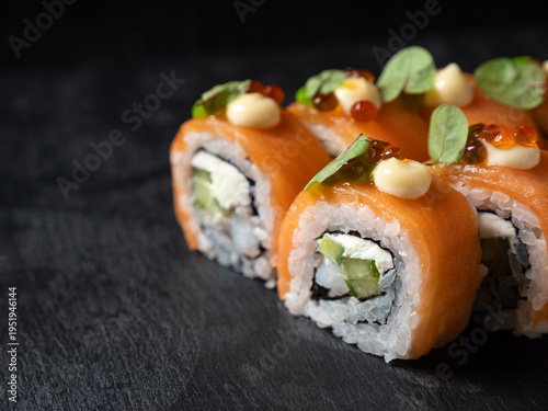 Japanese cuisine. Eating sushi roll with chopsticks  on a black platter