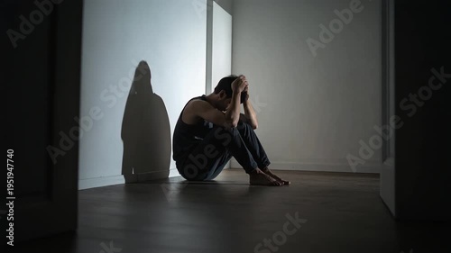 Adult man sitting on floor in dark room holding head showing deep emotional distress and mental health struggle indoors
