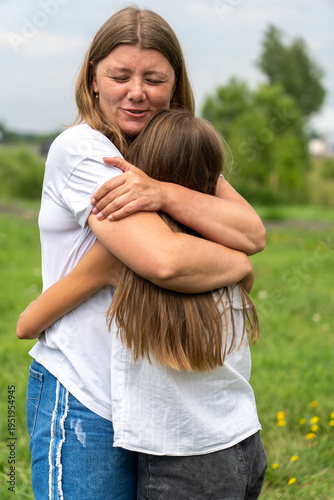 Tender moment of mother embracing her child closely outdoors in grassy field, sharing heartfelt hug with warmth and affection on slightly overcast day, promoting connection