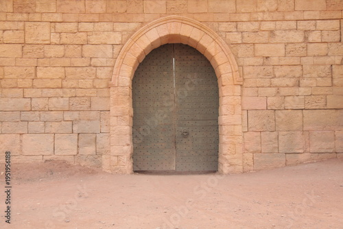 The Ancient Gateways of Atlas Film Studios.
This image captures a massive, arched wooden door built into a sun-baked sandstone wall in Ouarzazate, Morocco. Characterized by its rustic textures and met