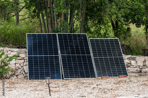 Three solar panels leaning against a rustic stone wall in a garden
