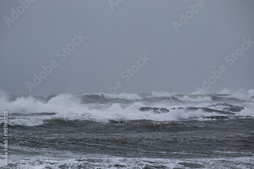 Powerful sea waves crashing against a rocky shoreline under a heavy overcast sky