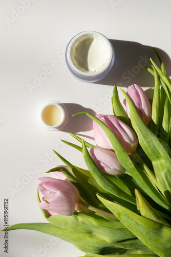 Closeup of a jar of moisturizer surrounded by tulips. Concept of spring skincare.