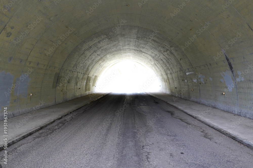 Obraz premium Symmetrical view of a bright light at the end of a dark concrete road tunnel portal