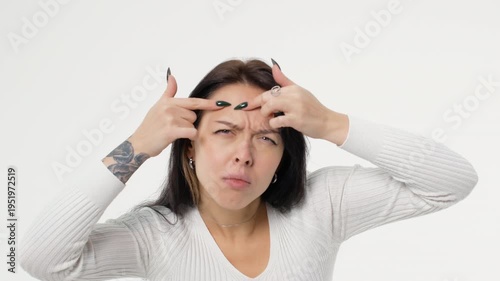 Young adult woman squeezes pimples and anxiously examines her face white background isolated space